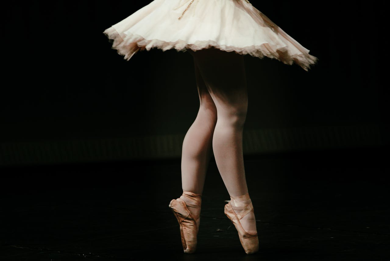 Close-up of a ballerina's legs in pointe shoes performing on stage, showcasing graceful movement.