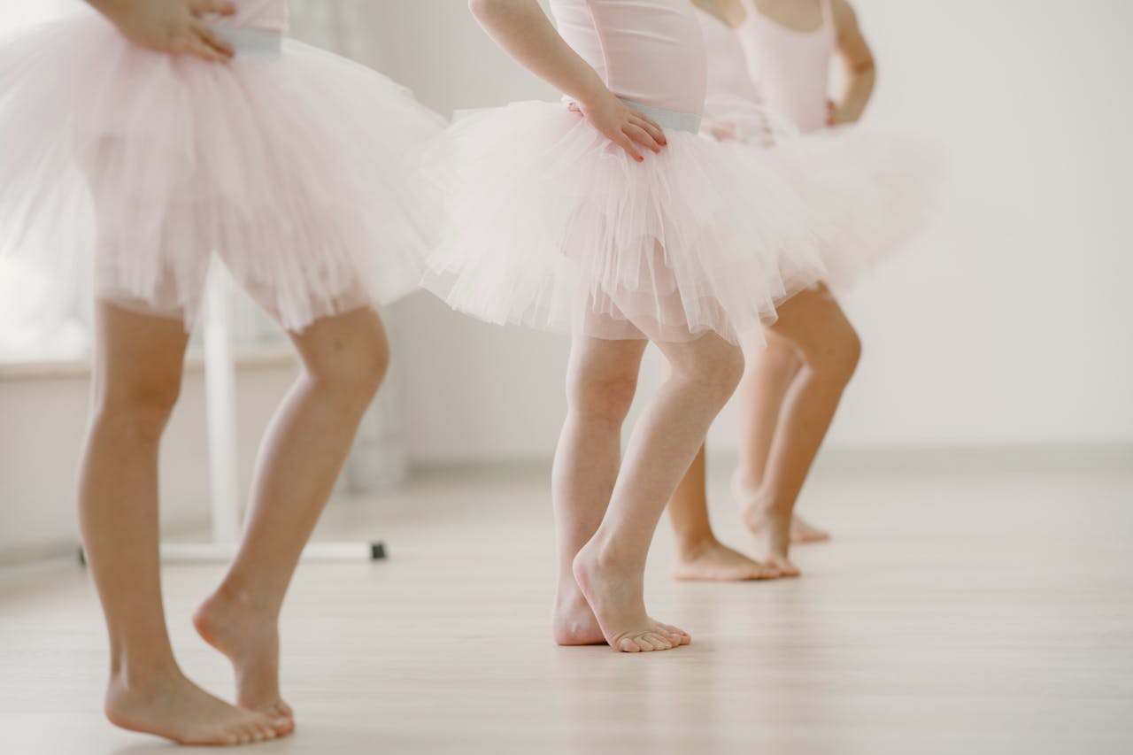 Close-up of young ballerinas in tutus practicing dance steps in a bright studio.